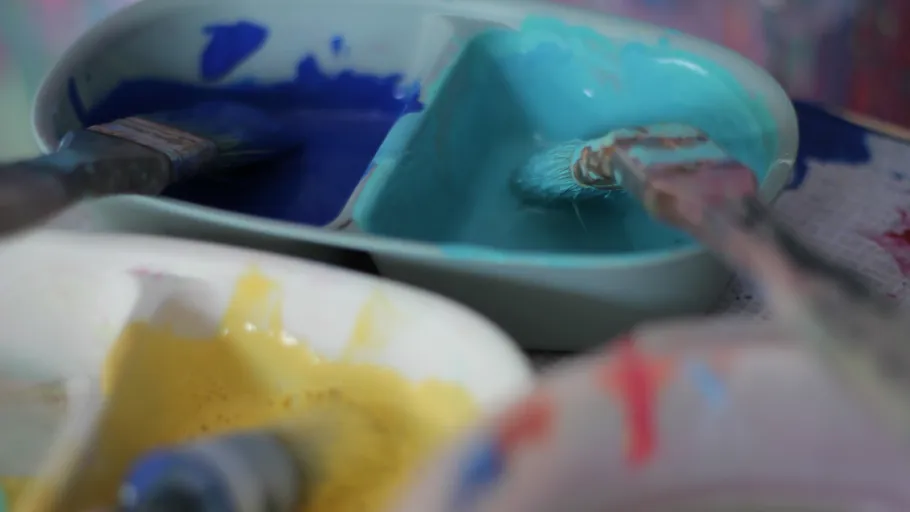 Pinsel in Schalen mit blauer und gelber Farbe.