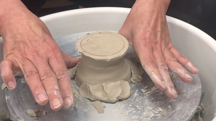 Hands sculpting clay on a pottery wheel.