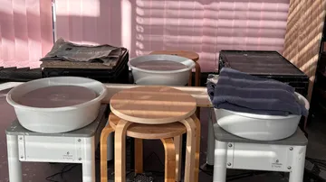 Plastikschüsseln, Hocker und Zeitungen auf Tisch.