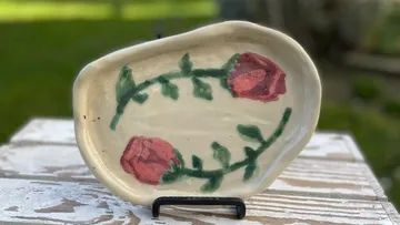 Hand-painted ceramic plate with rose design outdoors.
