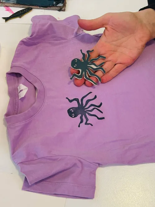 Hand holding octopus stencil on purple shirt.