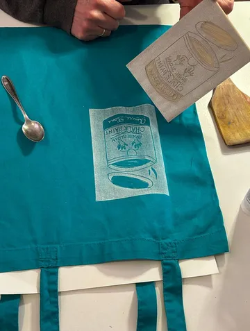 Hand überträgt Design auf türkisfarbenen Stoff mit Löffel.