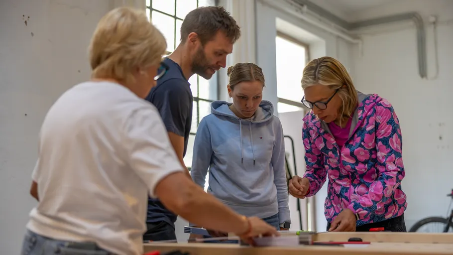 Vier Personen arbeiten gemeinsam an einem Tisch im Innenraum.