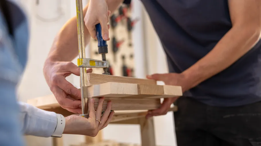 Two people clamping wooden boards together in workshop.