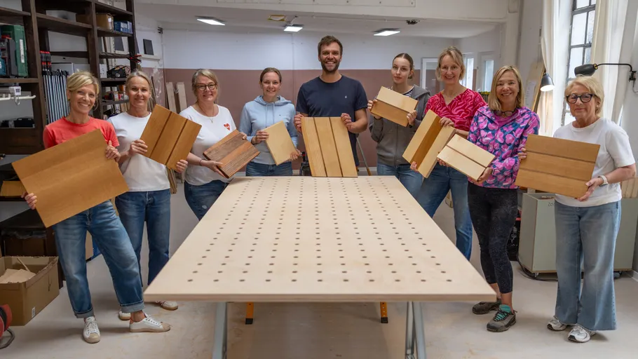 Group holding wooden boards in a workshop.