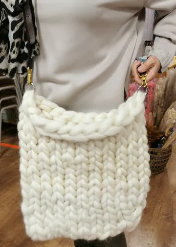 Hand holding chunky-knit white handbag indoors.
