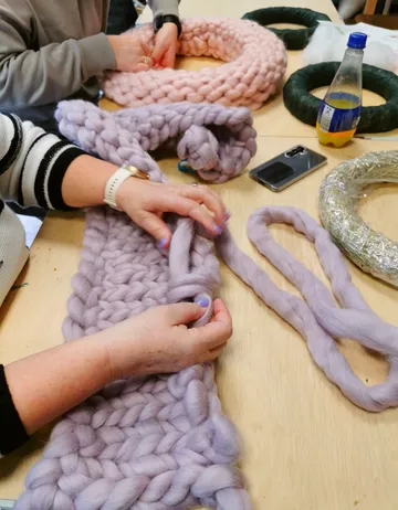 Hands knitting chunky wool on a table.