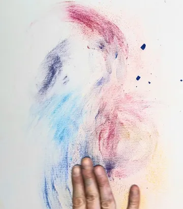 Hand blending colored chalk on white paper.