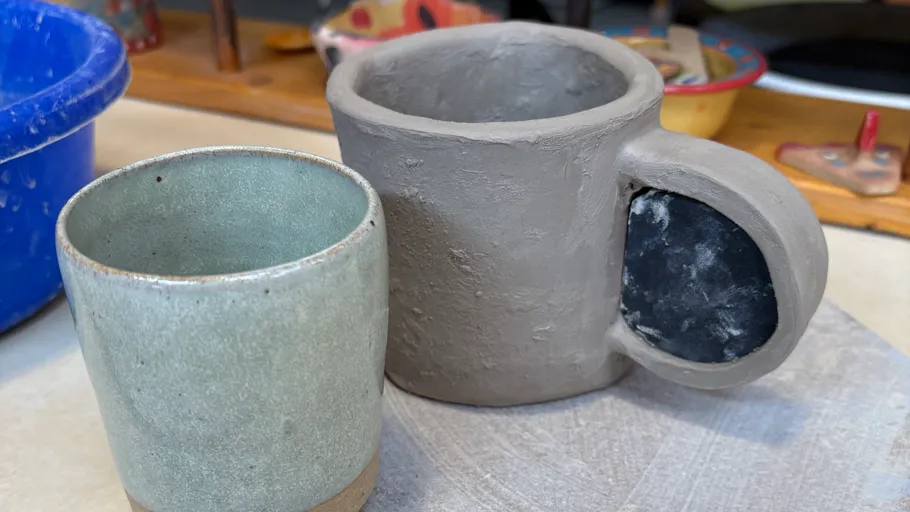Two unfinished ceramic mugs on a table.
