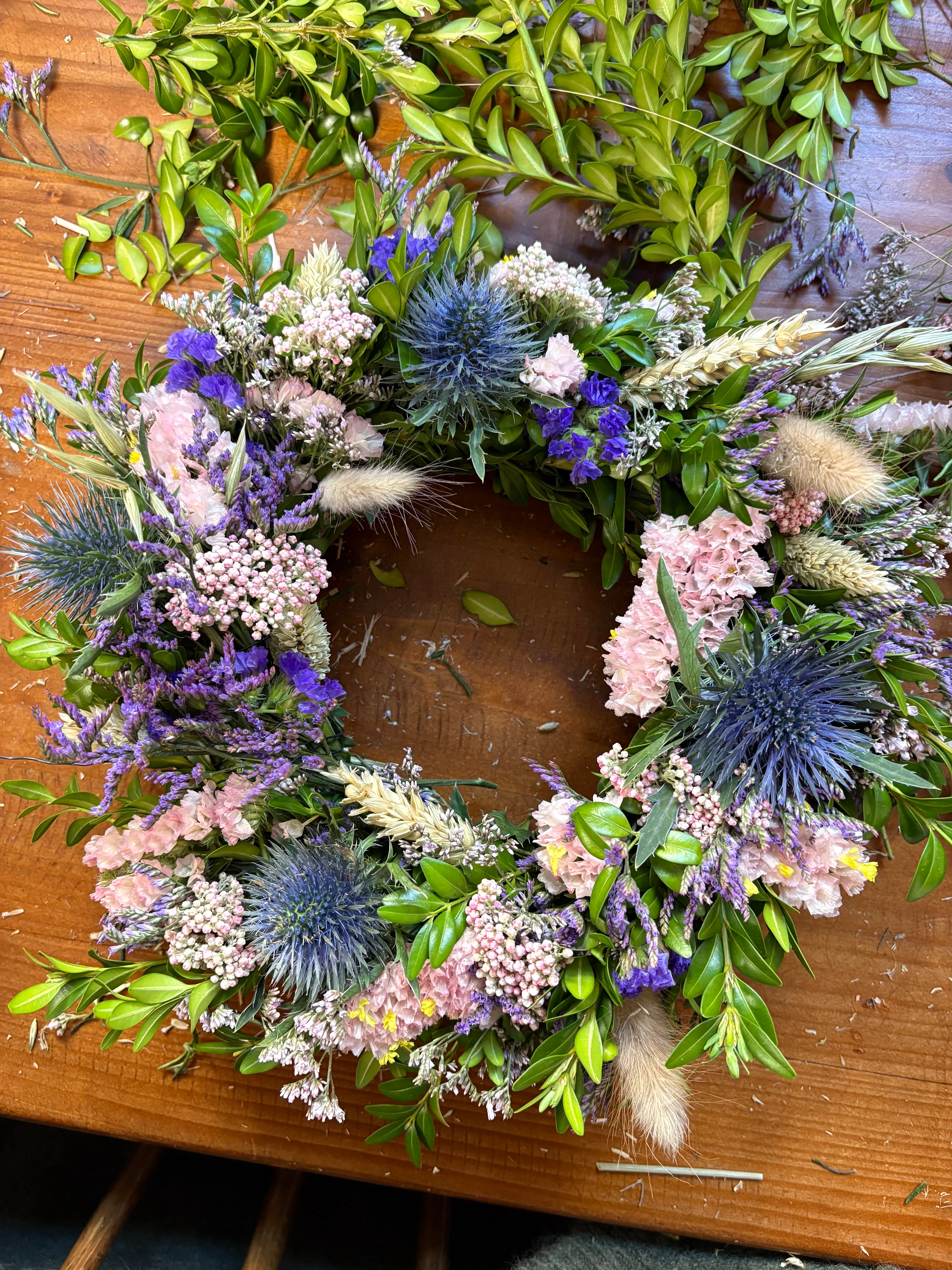 Floral wreath on wooden table with greenery.
