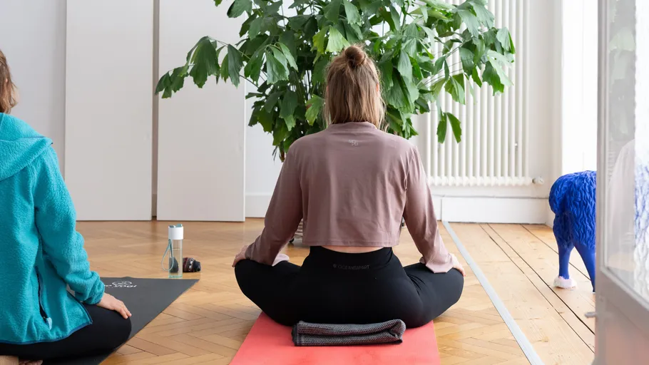 Zwei Personen meditieren auf Yogamatten drinnen.