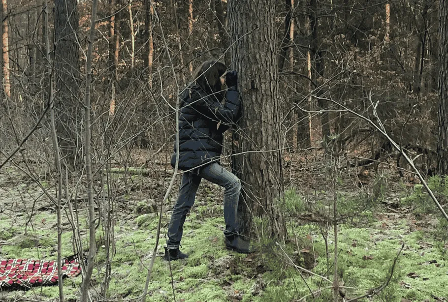 Person leaning against tree in forest.