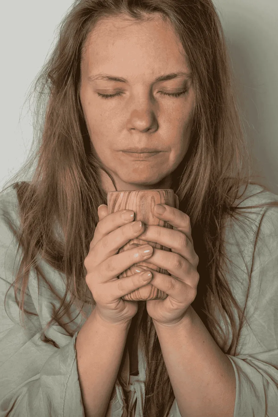 Woman holding cup, eyes closed, peaceful setting.