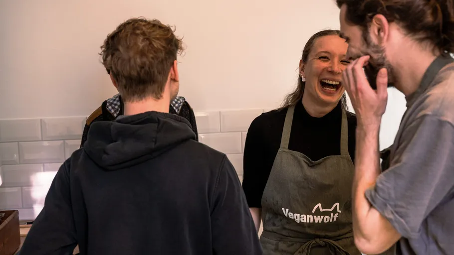 Menschen unterhalten sich, Frau in Veganwolf-Schürze lächelt.