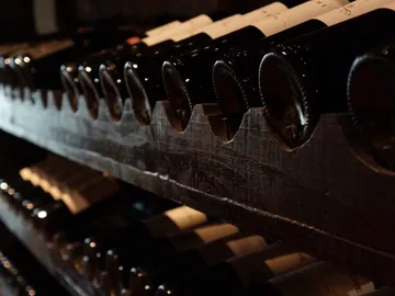Weinflaschen lagern auf einem Holzregal in einem Keller.