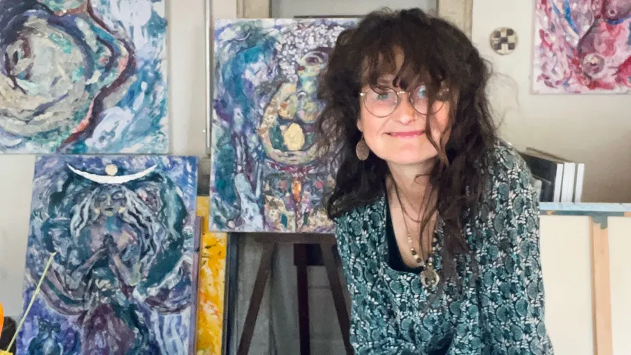 Artist smiling next to colorful abstract paintings.