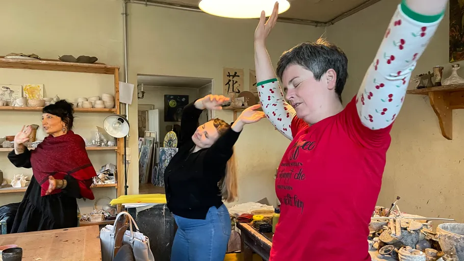 Three people dancing in a pottery studio.