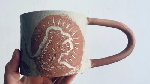 Hand holding mug with engraved rat design.
