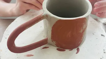 Clay mug being painted on a table.