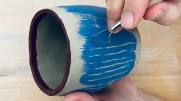 Hand kratzt blaue Farbe von einem Tontopf.