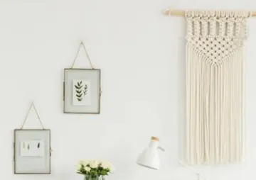 Makramee hängt an der Wand, mit Bildern und Blumen daneben.