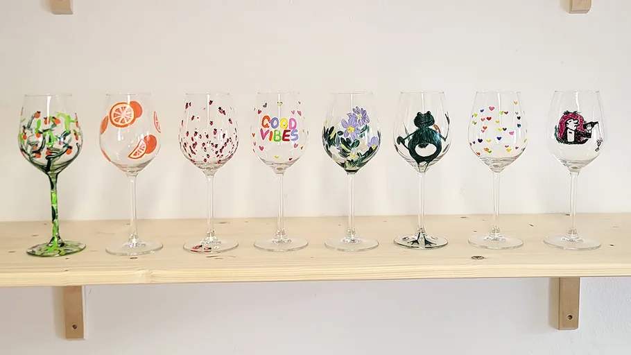 Seven painted wine glasses on wooden shelf.
