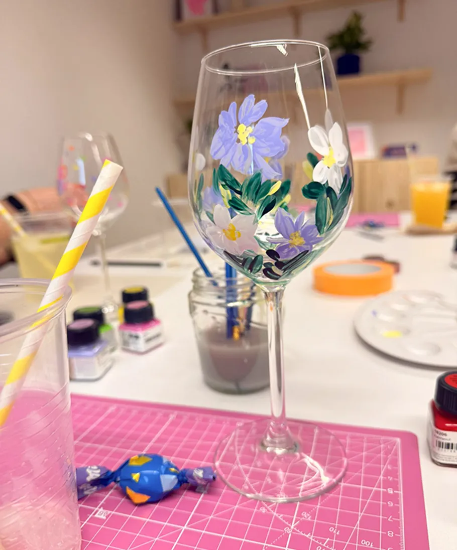 Painted wine glass with floral design, crafting supplies.