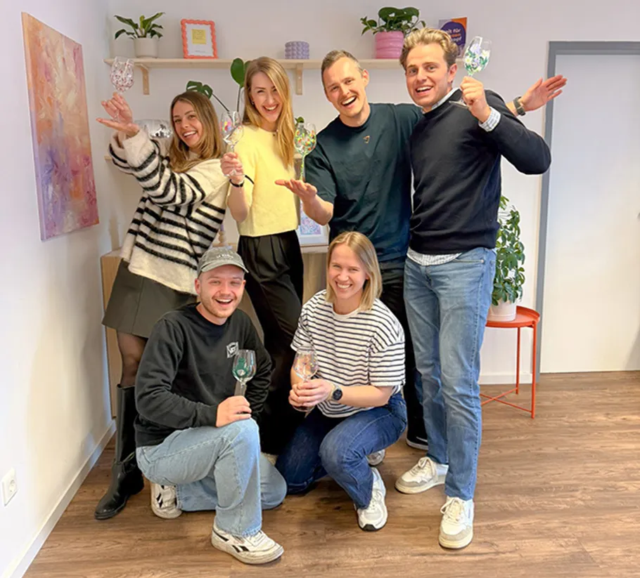 Group of six people holding glasses, indoors.