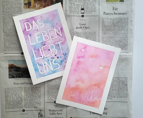 Two watercolor cards on a newspaper background.