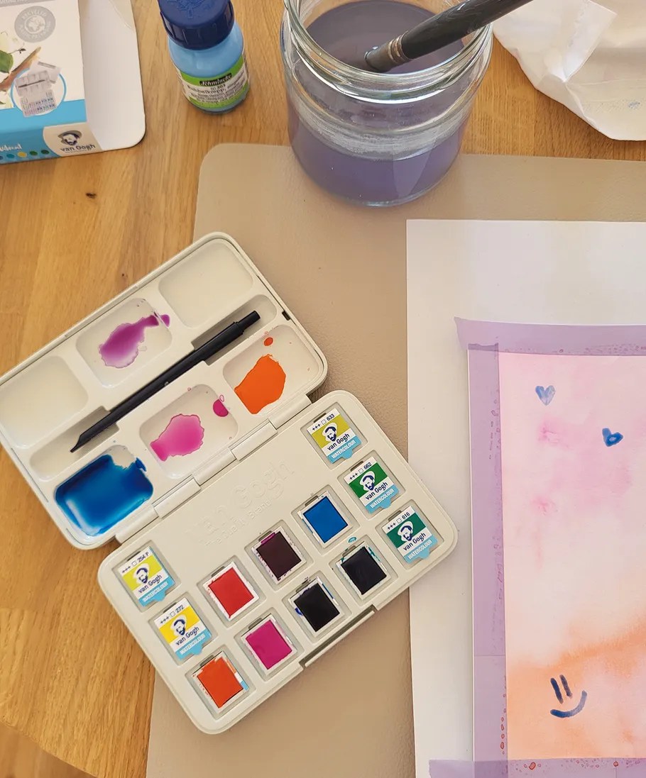 Watercolor set, brush, painting on wooden table.