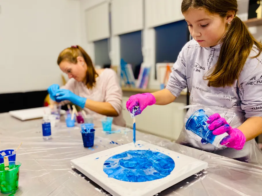 Two girls creating art with blue paint indoors.