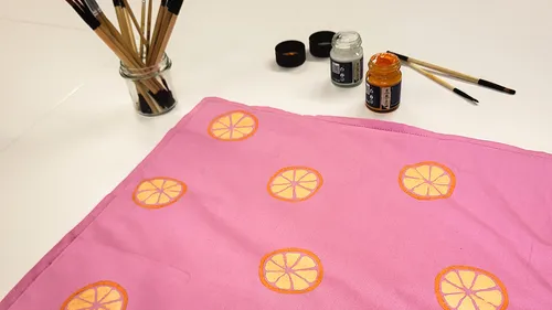 Rosa Stoff mit orangenen Mustern, Malutensilien in der Nähe.