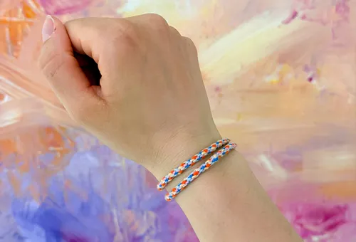 Hand wearing colorful bracelet against painted background.