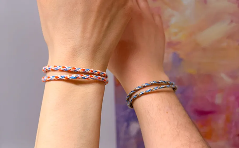 Two hands wearing colorful braided bracelets.