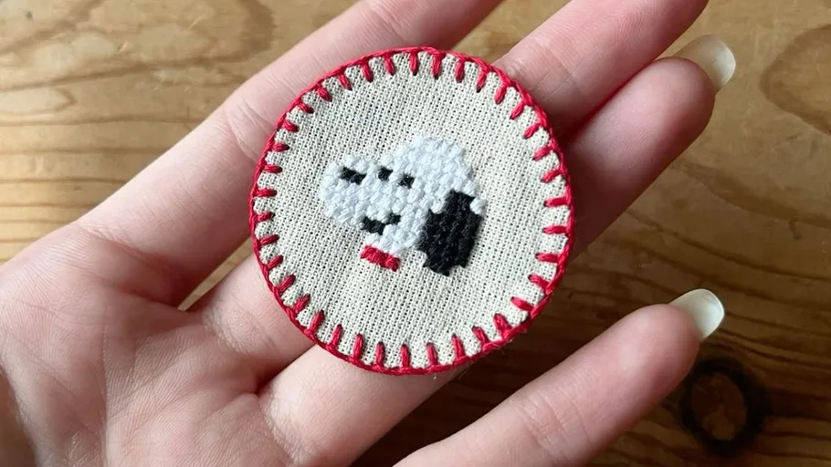 Hand holding embroidered patch with dog design.