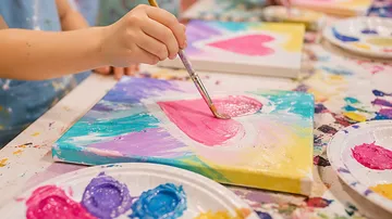 Child painting pink heart on canvas.