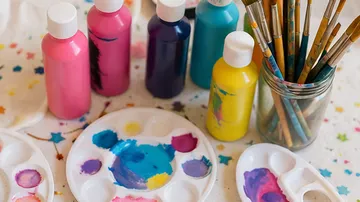 Paint bottles and brushes on a colorful table.