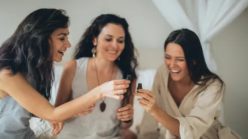 Drei Frauen lächeln, halten kleine Flaschen drinnen.