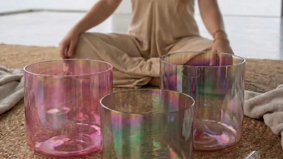 Woman sitting with colorful singing bowls indoors.