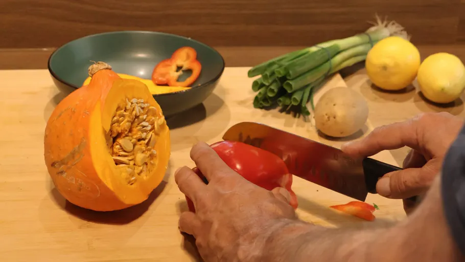 Person schneidet rote Paprika auf der Arbeitsplatte.