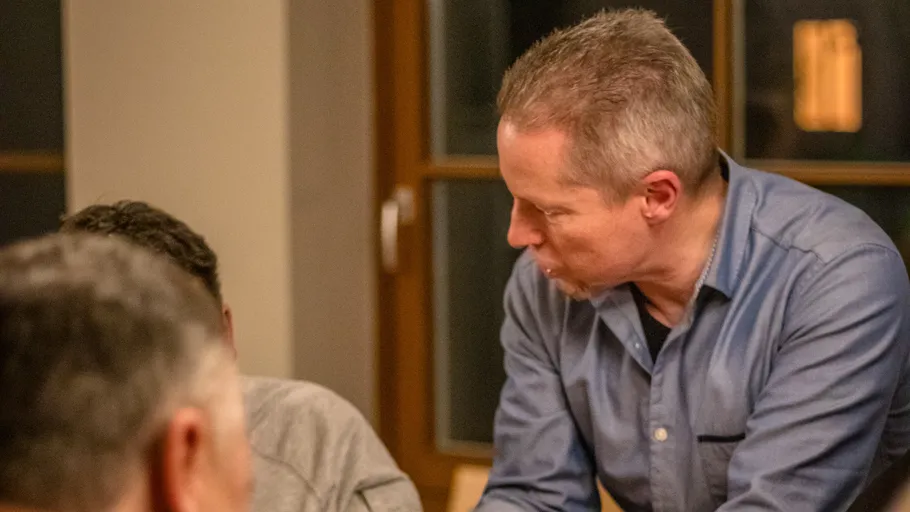 Man in blue shirt talking to seated people.
