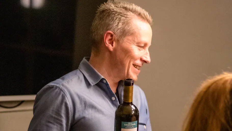 Man smiling, holding a wine bottle indoors.