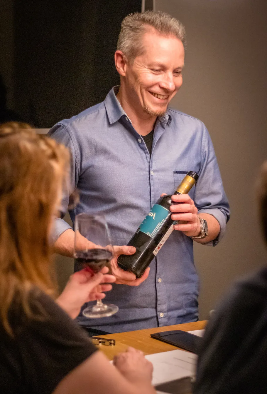Man presenting wine bottle in social setting.