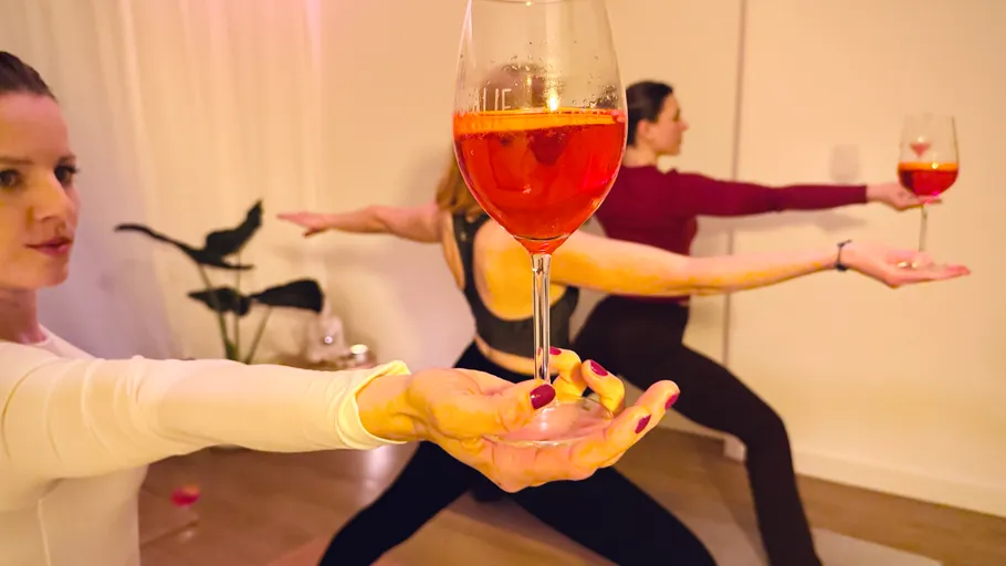 Frauen machen Yoga, halten Getränke, drinnen.