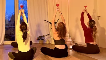 Drei Frauen machen Yoga und halten Weingläser.
