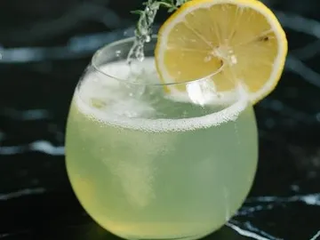 A drink with lemon is poured into a glass.