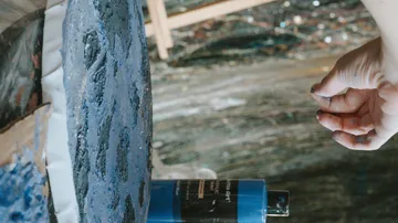 Hand greift nach blau bemalter Leinwandkante.