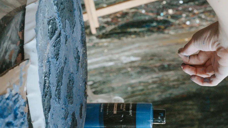 Hand greift nach blau bemalter Leinwandkante.
