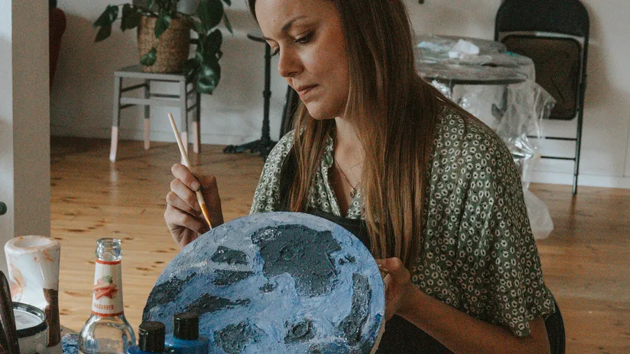 Frau malt blaues Kunstwerk im Raum.