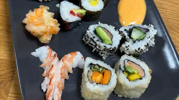 Verschiedene Sushi-Rollen auf einem schwarzen Teller.